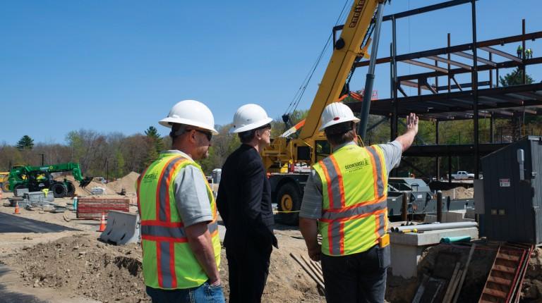 Three construction workers wearing hard hats examine the construction of the new U N E portland campus medical school building